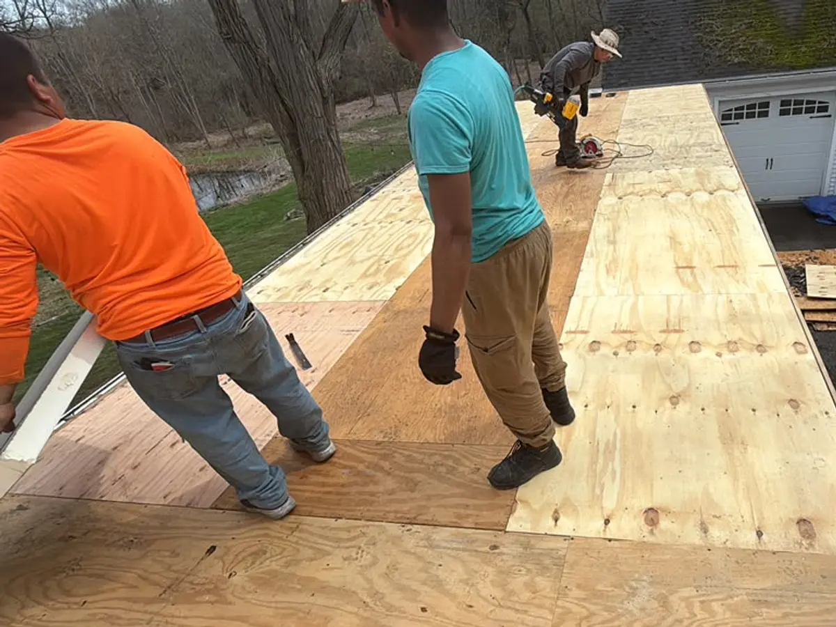Two roofers laying new plywood decking on a flat roof