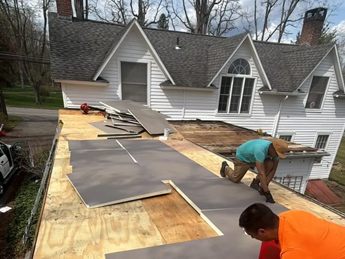 Crew working across a low-slope roof beside a white residential house