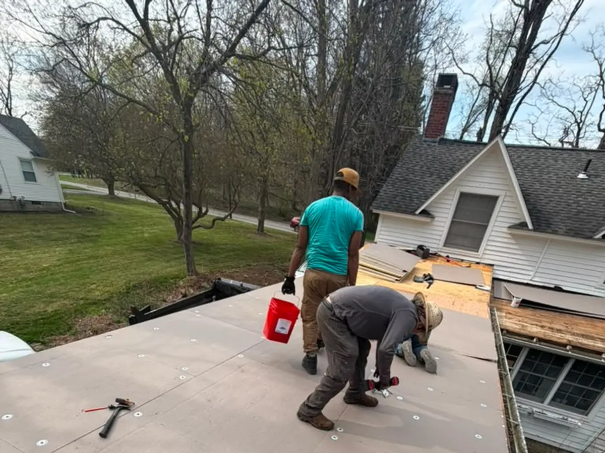 Roofers stripping shingles from a steep roof against a bright blue sky