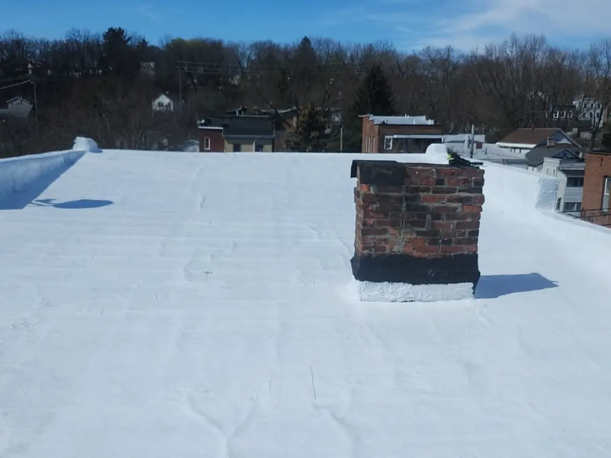 White-coated flat roof with a brick chimney, rooftops of the surrounding neighbourhood behind