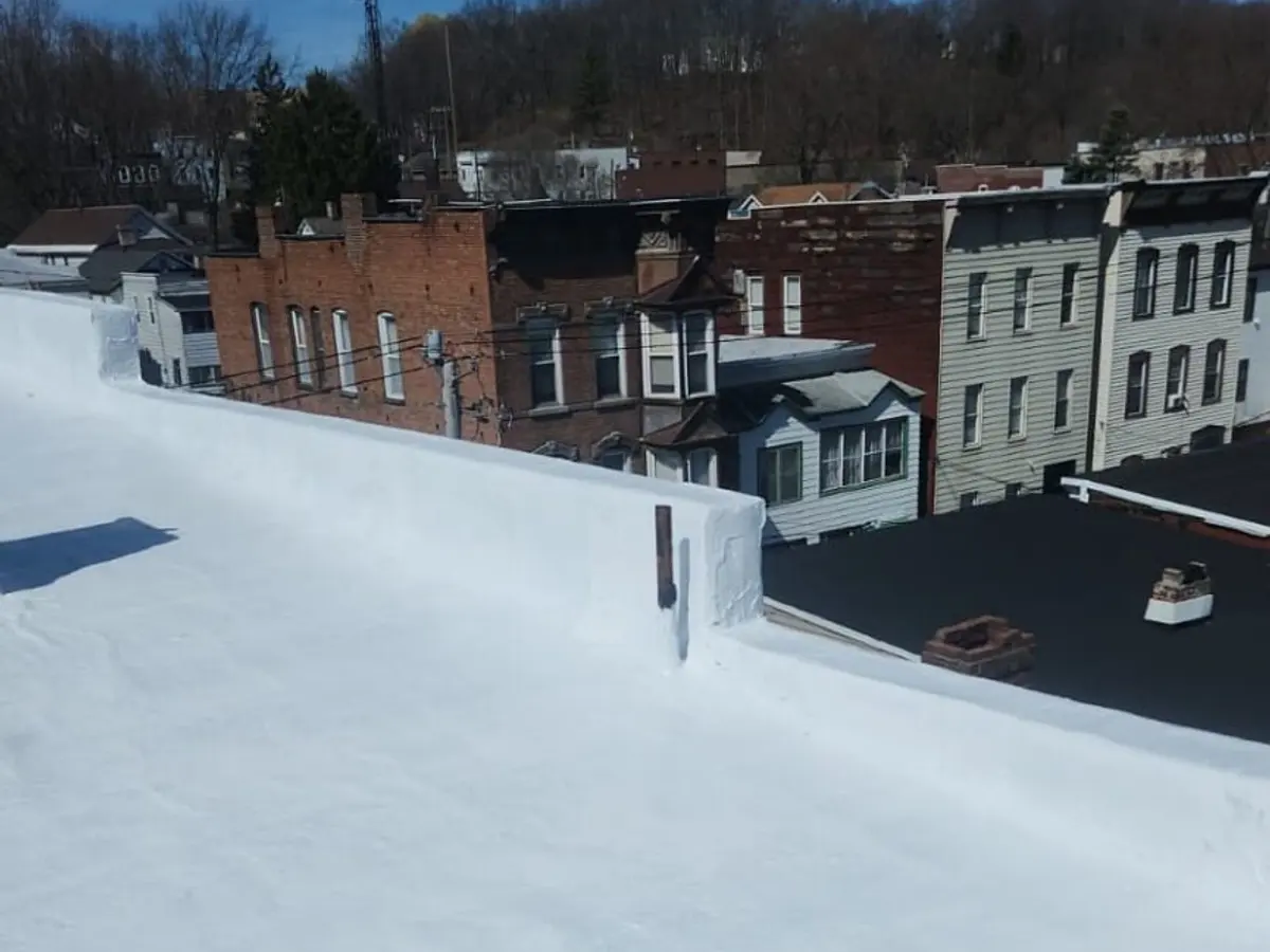 Freshly coated flat roof under a clear blue sky, chimney sealed at the base
