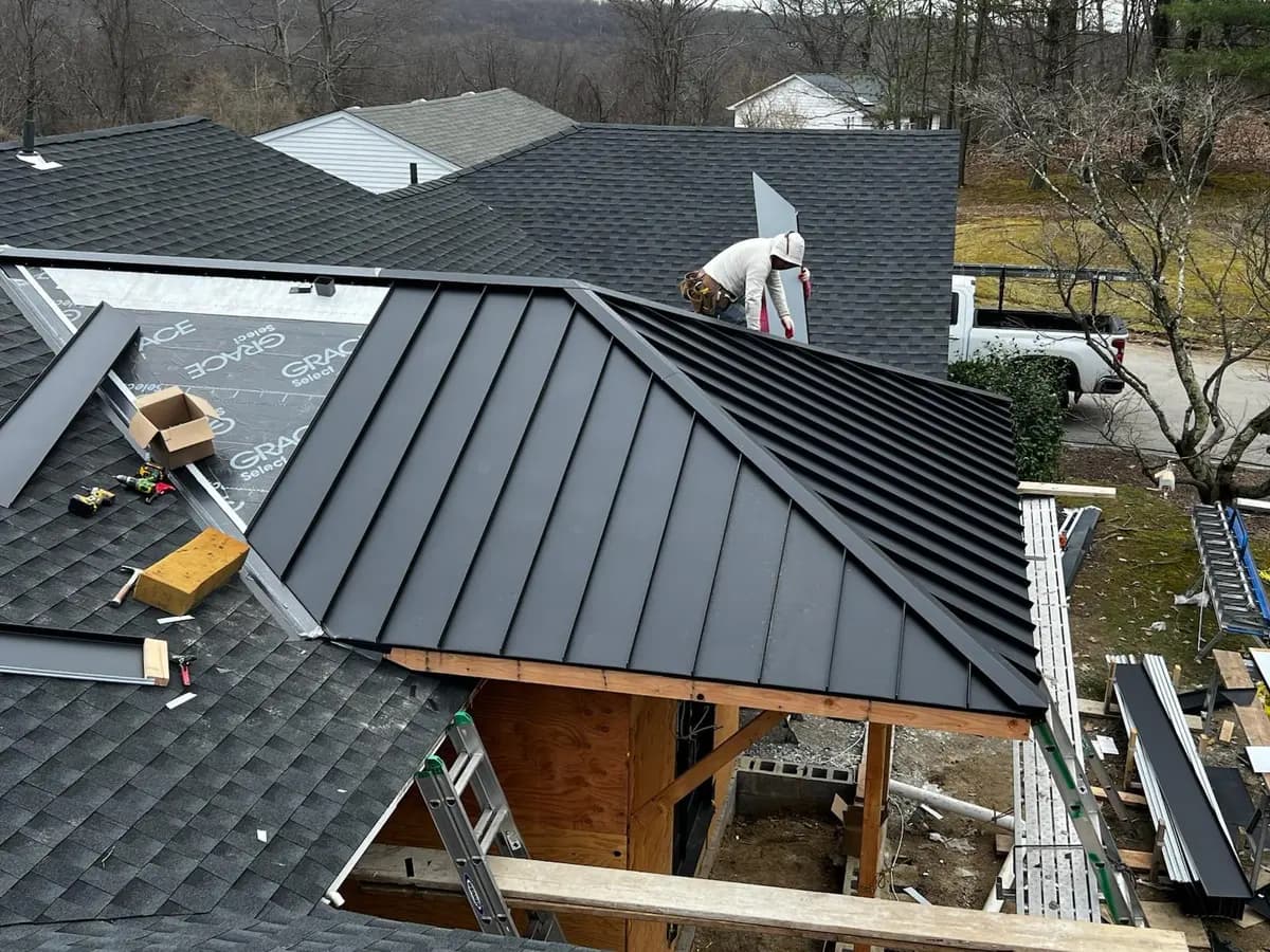 Dark standing seam metal roof over a timber-framed extension, still under construction