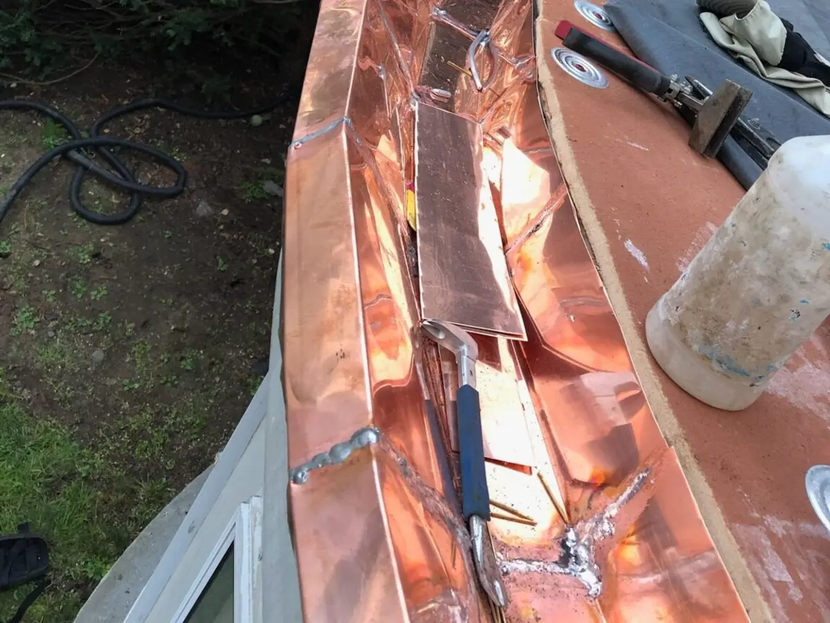 New copper flashing stepped into a brick chimney beside slate shingles