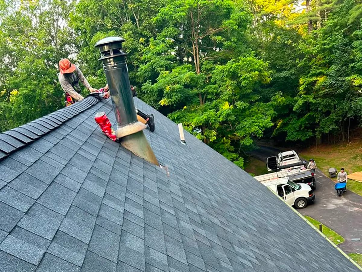 Roofer fitting a ridge vent along the peak of a newly shingled dark grey roof