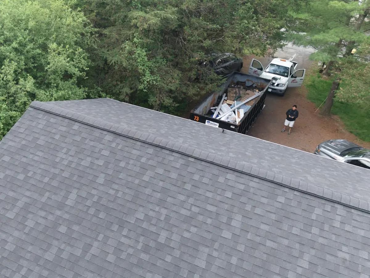Finished grey architectural shingle roof photographed from the ridge, work trucks parked below