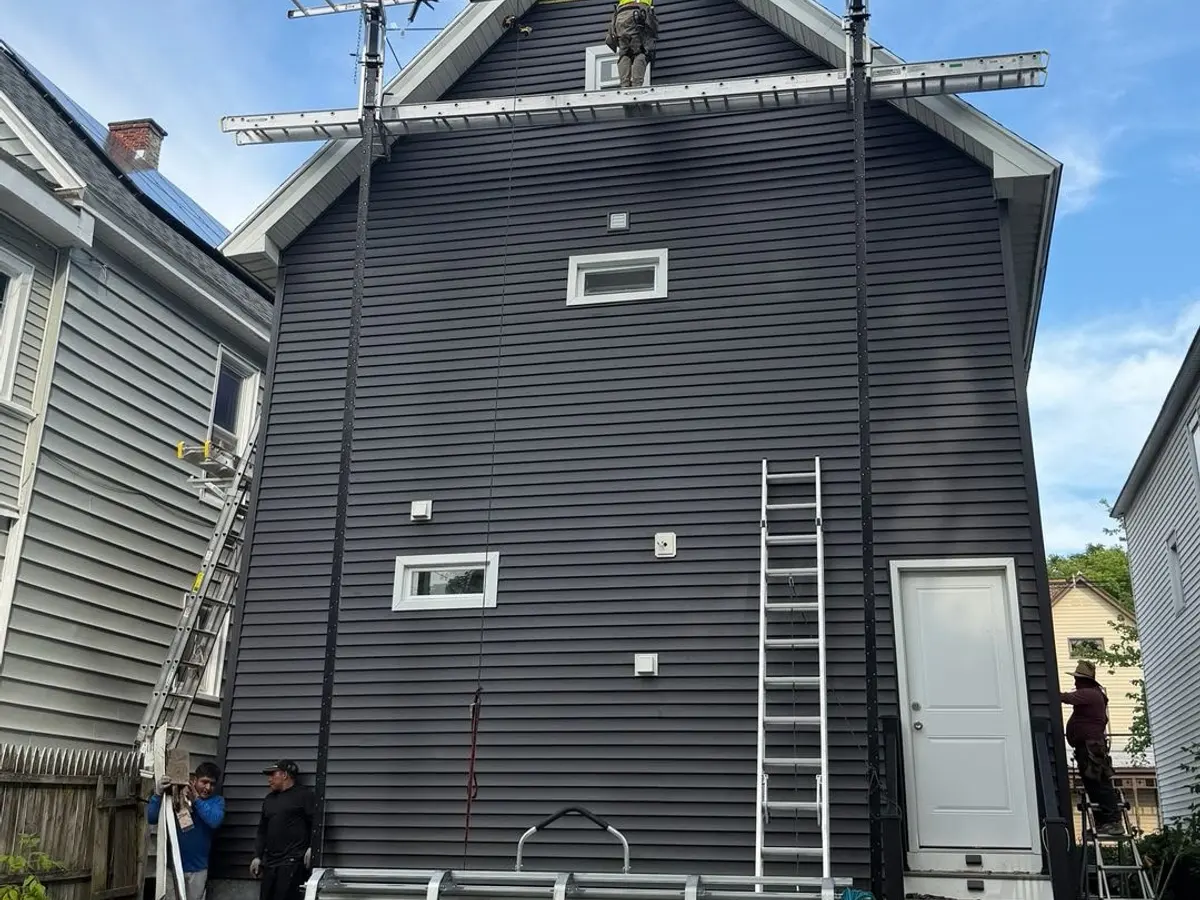 Tall home finished in dark charcoal siding, ladder still against the wall